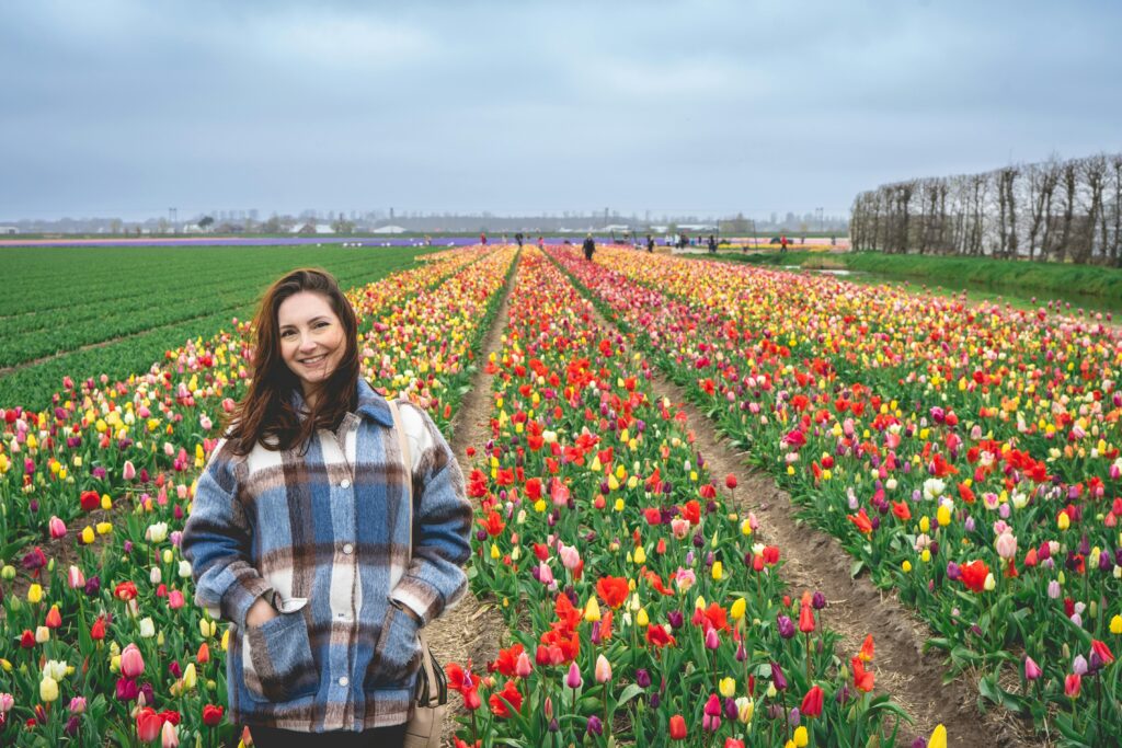 A cheerful woman poses in vibrant tulip fields in Hillegom, Netherlands, capturing the essence of spring.
