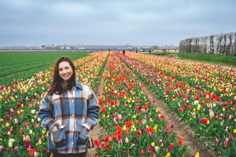 A cheerful woman poses in vibrant tulip fields in Hillegom, Netherlands, capturing the essence of spring.